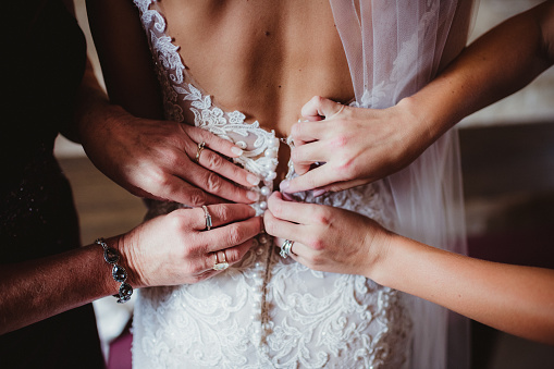Mother and grandmother's hands buttoning the bride's wedding dress