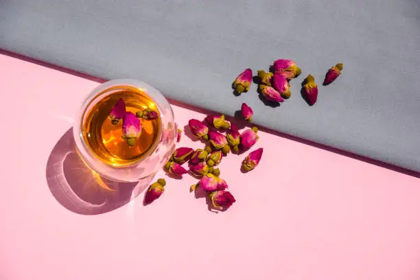 Tea with rosebuds. Dry rosebuds, a teacup on a pink background. dried rosebuds on a pink surface. Herbal tea made from dried pink rosebuds in a glass mug.