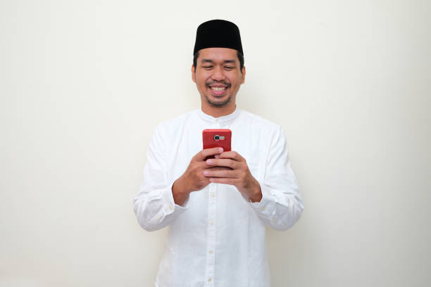 Moslem Asian man smiling happy when texting using his mobile phone Moslem Asian man smiling happy when texting using his mobile phone keluarga stock pictures, royalty-free photos & images