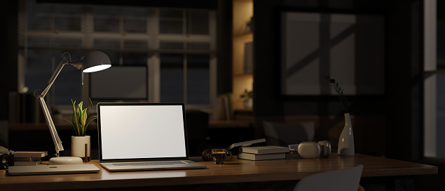 close-up image, Home workspace at night with laptop white screen mockup, light from table lamp and stuff on table over blurred darkness room in background. 3d render, 3d illustration