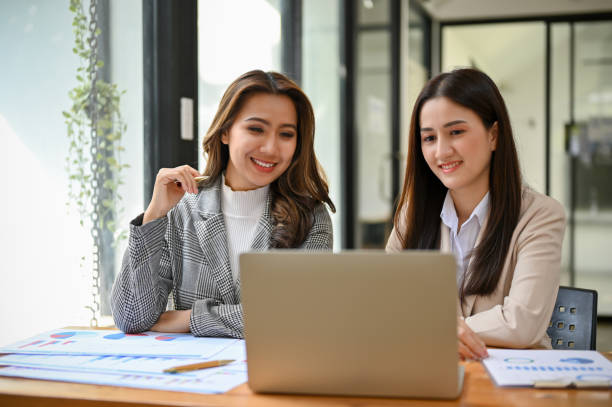 istock Two beautiful millennial Asian office workers working together, looking at laptop screen 1457809576