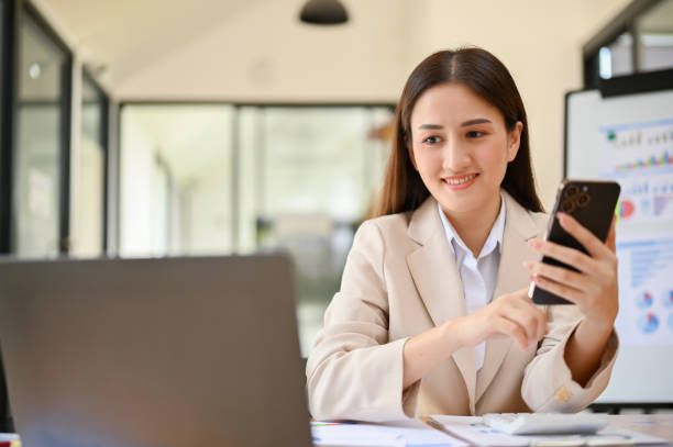 istock Charming millennial Asian businesswoman looking at laptop screen while using her phone 1457809628