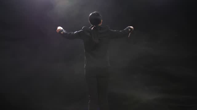Back View Of Asian Conductor Woman Holding A Baton And Showing Gesture In The Black Studio With Fog