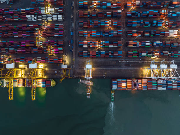 istock aerial top view international shipping port load and unloading container by crane onto transport ships and trailer for import export distributing products to customers and consumer over lighting at night scene 1457824457