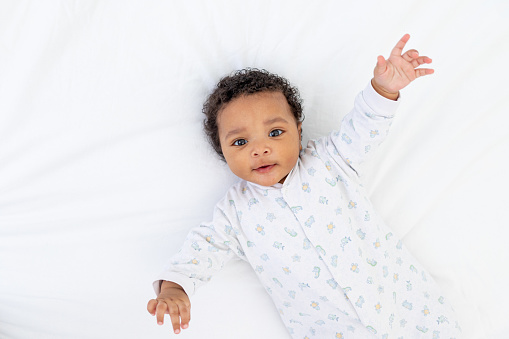 An African-American young child on a white bed in the bedroom is lying in his pajamas