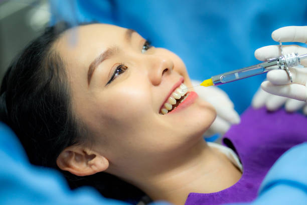 도구와 주사기를 손에 들고 있는 치과 의사의 손을 닫습니다. 진통제가 작동합니다. 여성 클라이언트는 입을 벌리고 있습니다. - dentist dental assistant dentist office dental drill 뉴스 사진 이미지