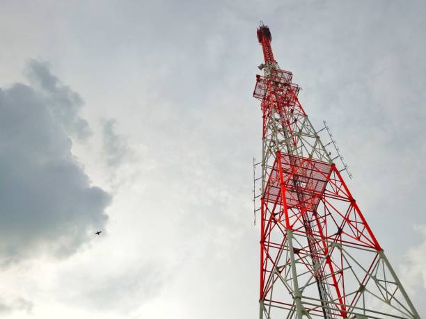 Red and white telecommunication tower reaching high into a cloudy sky, broadcasting signals across the landscape