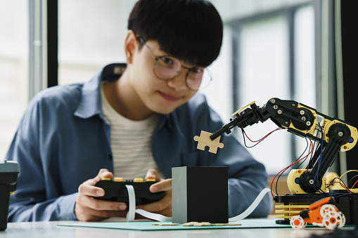 Asian teenager students doing or playing robot arm and robotic cars homework project in house assemble the circuit and coding. technology of robotics programing and STEM education concept