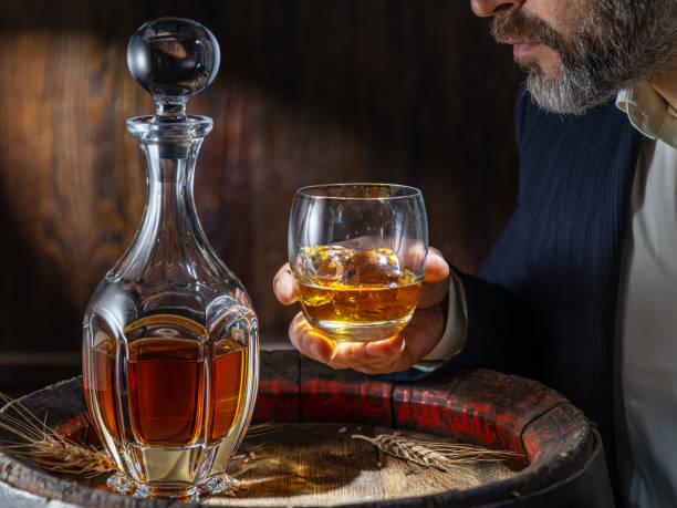 degustazione di whisky. l'uomo si siede davanti a una botte con un decanter e un bicchiere di whisky. - gin decanter whisky bottle foto e immagini stock