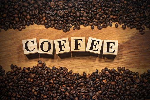 Large group of roasted coffee beans on a wooden background and the text Coffee, made of wooden blocks. Photography.