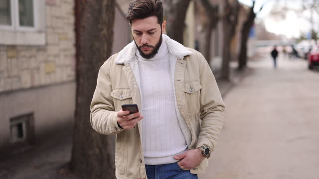 Attractive young man listens to voice mail while walking in the city