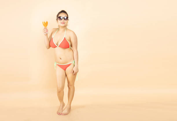 schöne junge brünette indische mädchen schlanker körper tragen roten bikini und sonnenbrille genießen glas von orange dink isoliert auf beigem hintergrund, studioaufnahme. tropische sommer-strandparty und urlaubskonzept. - party beach indian ethnicity adult stock-fotos und bilder