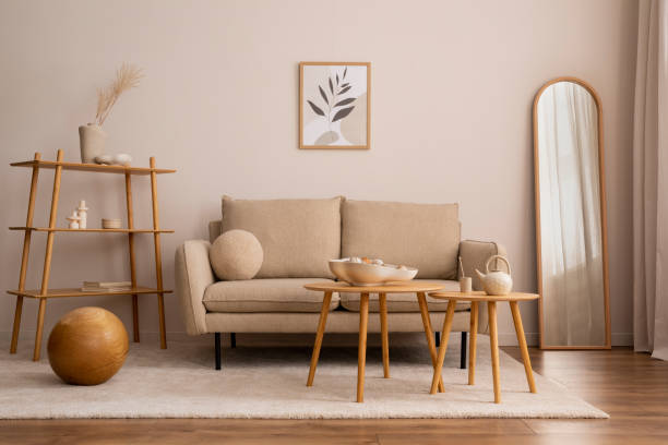 istock Creative composition of living room interior with mock up poster frame, classic beige sofa, wooden round coffee table, mirror, elegant bowl and stylish personal accessories. Beige wall. Home decor. Template. 1457867370