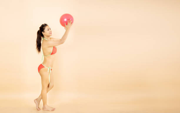 playful young asian indian woman slim body wearing red bikini hold play beach ball isolated on beige background, studio shot. summer holidays and travel concept. - party beach indian ethnicity adult imagens e fotografias de stock
