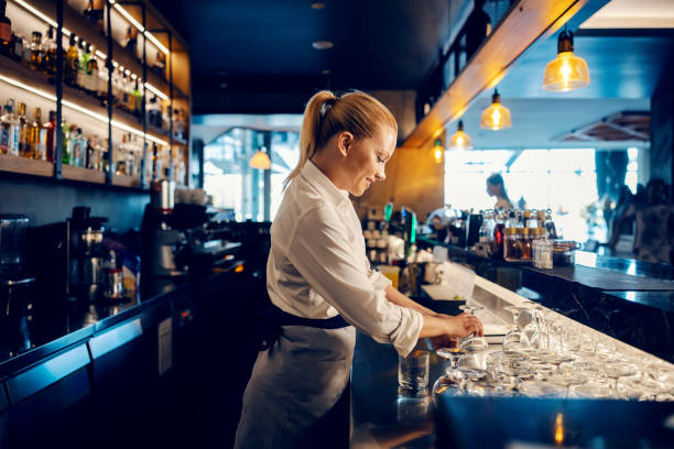 A bartender is working with clean glasses behind a counter in a bar. stock photo