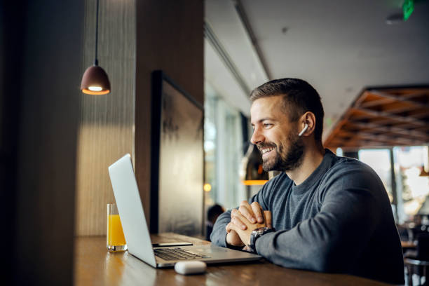 A friendly freelancer is sitting in a coffee shop and having conference call with client. stock photo