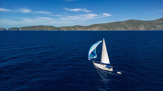 Aerial view of sailboat sailing and navigating at with slow morning breeze power using spinnaker. Photo taken with drone