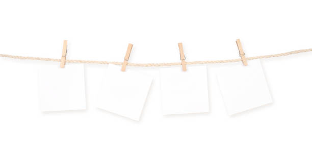 Four White Notepads Hanging on Rope. Isolated with Path. Four blank square notepads reminders and clothespins attached to a rope on white background. Clipping Path Included. clothespin wood stock pictures, royalty-free photos & images