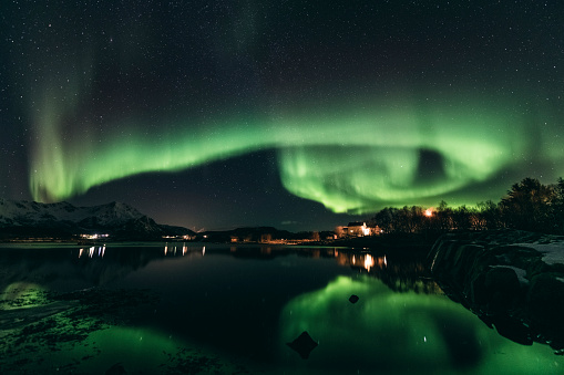 Northern Lights, polar light or Aurora Borealis in the night sky over the Vesteralen islands in Northern Norway. Panoramic image with snow covered mountains and a lake in the foreground.