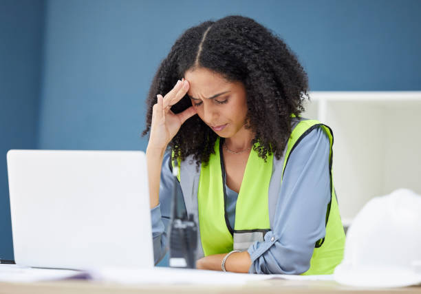 istock Construction, stress and woman engineer at laptop, architect or contractor in office with headache from work. Burnout, anxiety and deadline for building project, black woman in safety vest at desk. 1457871297