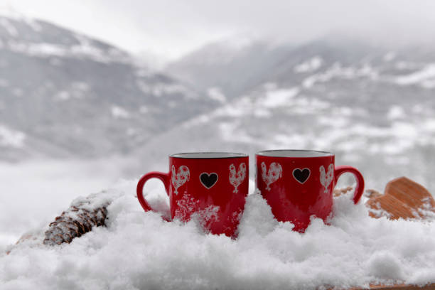 istock two red mugs with heart shaped on the snow and mountain background 1457873247