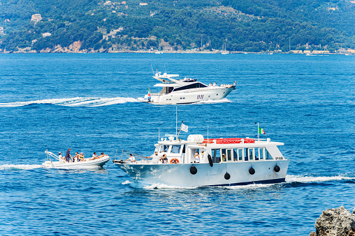 La Spezia, Italy - July 16, 2022: White motor boats in the blue Mediterranean Sea on a sunny summer day, a ferry, a dinghy and a luxury yacht with people on board. Gulf of La Spezia, La Spezia, Liguria, Italy, Europe.