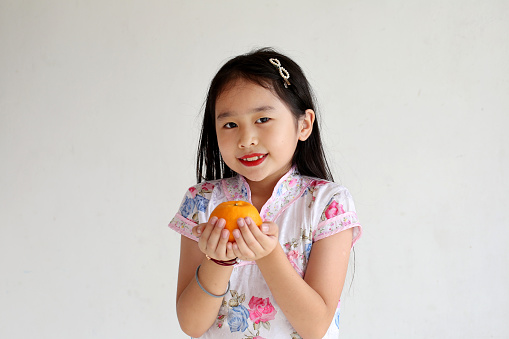 Portrait of Asian girl in traditional Chinese cheongsam attire and holding mandarin orange fruit.