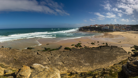 Panoramic landscape of the Atlantic ocean beach of Praia das Macas. View of great waves of a powerful ocean break into foam and surfers on a sandy long beach. Portugal.