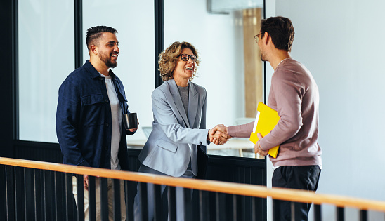 Professional woman shaking hands with a new employee in an office. Happy business woman hiring a job candidate. Business people forming a new partnership in a startup.