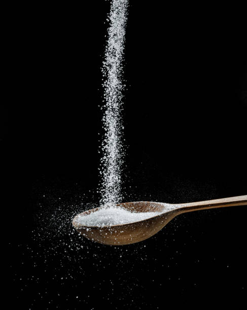 istock White refined sugar crystals falling down into the wooden spoon at black background. 1457883134