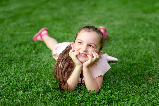 a 5-6-year-old girl lies in the Park on the grass and laughs, happy childhood, child's day