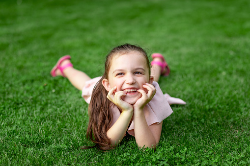 A small beautiful blonde girl in a blue linen sundress against a background of tall grass