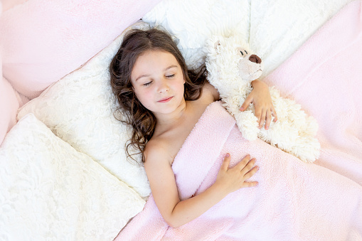 beautiful little girl 5-6 years old sleeping in a bed with a Teddy bear