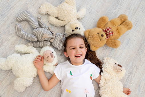 a little girl 5-6 years old lies among Teddy bears