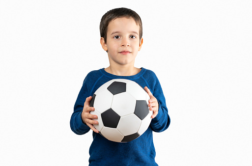 Dark haired little child playing with soccer ball with a happy face standing and smiling with a confident smile with white background