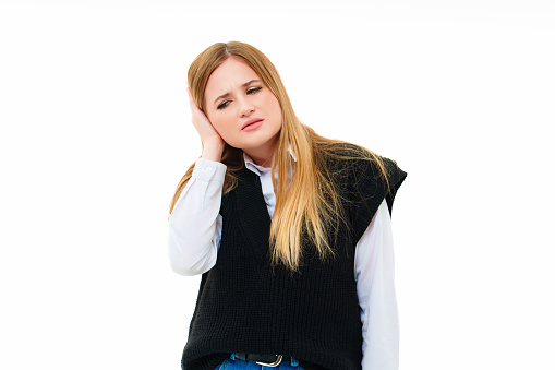 a blonde in a black knitted vest keeps hand on ear on a white background. ent disease, migraine or headache. the concept of drugs and painkillers. advertising of clinic, pharmacology or pharmacy