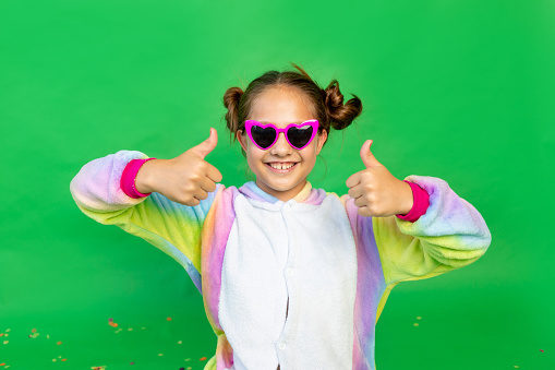 a little girl on a green isolated background in a bright suit and glasses shows her thumbs up. Space for text. The concept of a holiday, Birthday and sales