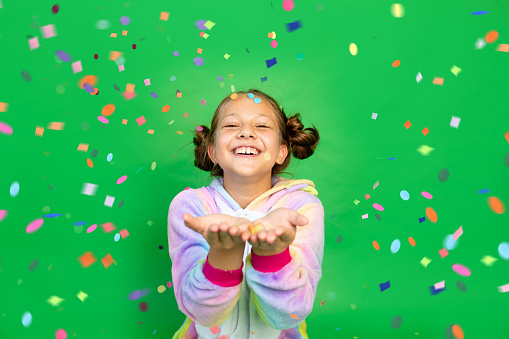 a little girl on a green isolated background in a bright suit blows away a streamer. Space for text. The concept of a holiday, Birthday and sales