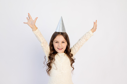 A young girl on her birthday as a Princess in a hat with her arms outstretched screaming on an isolated white background, a young beautiful girl smiling with a happy face