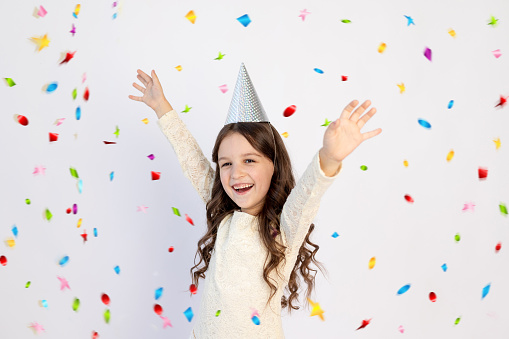 A young girl on her birthday as a Princess in a hat with her arms outstretched screaming on an isolated white background, a young beautiful girl smiling with a happy face
