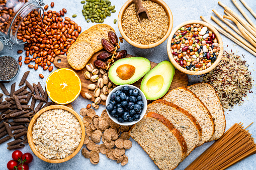 Overhead view of a large group of food with high content of dietary fiber. The composition includes berries, oranges, avocado, chia seeds, wholegrain bread, wholegrain pasta, whole wheat, potatoes, oat, corn, mixed beans, brazil nut, sunflower seeds, pumpkin seeds, broccoli, pistachio, banana among others. High resolution 42Mp studio digital capture taken with SONY A7rII and Zeiss Batis 40mm F2.0 CF lens