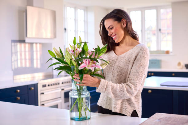 ガラスの花瓶に花束を並べる家で微笑む女性 - flower arranging ストックフォトと画像