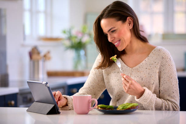istock Woman At Home With Digital Tablet On Kitchen Counter Eating Lunch 1457891378