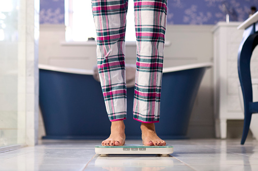 Close Up Of Woman At Home Wearing Pyjamas Weighing Herself On Bathroom Scales