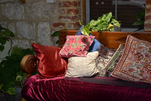 Shabby chic outdoor couch or settee with velvet cushions and a shaft of sunlight on the distressed brick wall in the background