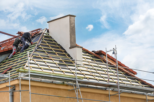 view on unfinished building and roofers with professional tools installing wooden framework from planks on roof on blue sky background