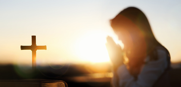 The red sunset light background, the Holy Bible, the cross of Jesus, and a Christian praying with both hands together