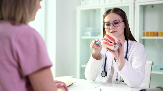 Doctor dentist shows how to properly brush teeth of female patient with dental implants