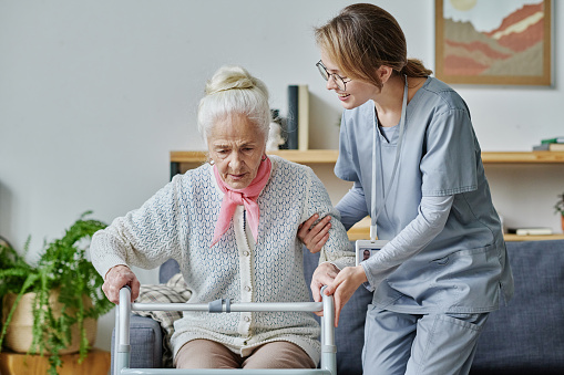 Young volunteer working in nursing home, she helping senior woman to stand using walker