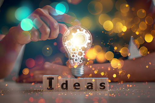 hand touching on light bulb on wood block with Word Ideas, new idea concept with innovation and inspiration, innovative technology in science and communication concept.